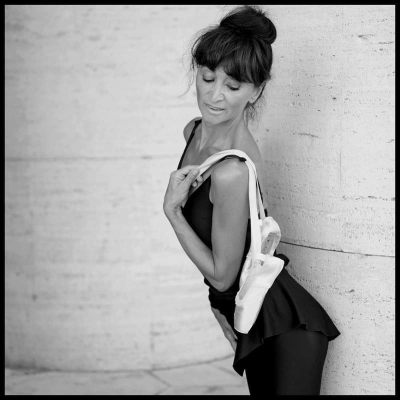 Donna in abbigliamento elegante, in posa artistica accanto a una colonna, con un'espressione contemplativa.