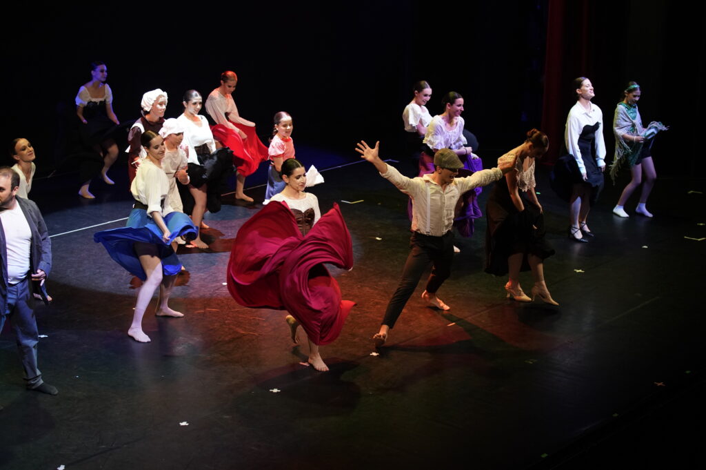 Gruppo di ballerini in abiti colorati si esibisce su un palco, mostrando movimenti coreografici dinamici.