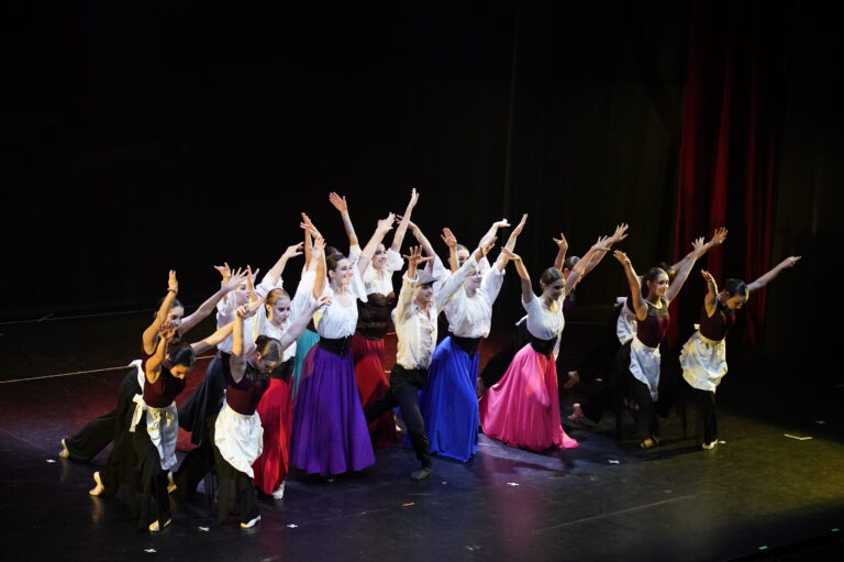Gruppo di ballerini in abiti tradizionali, in pose dinamiche sul palco durante una performance.