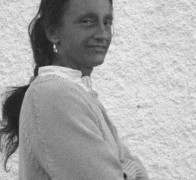 Donna con capelli lunghi e scuri, indossa un maglione chiaro e guarda verso l'osservatore con un sorriso.