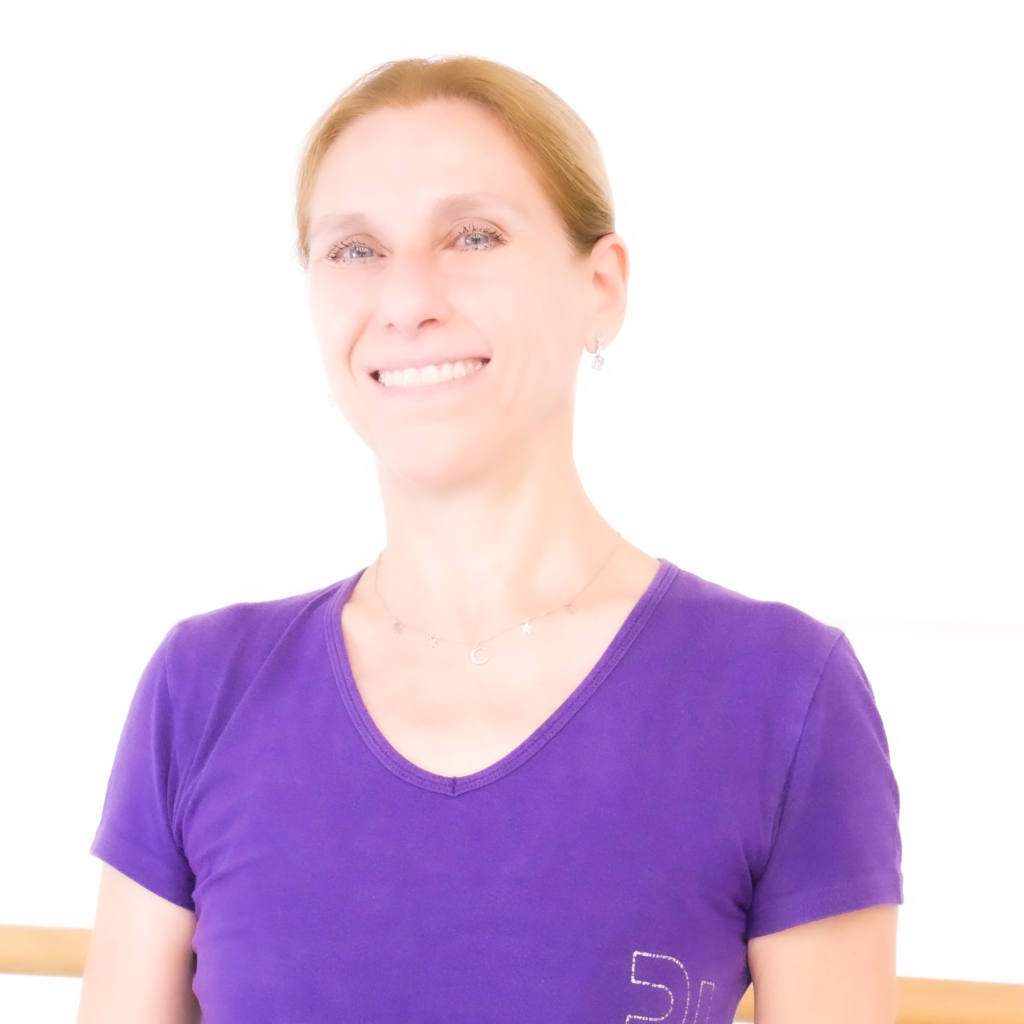 Donna sorridente con maglietta viola, capelli lunghi e lisci, in un ambiente luminoso e minimalista.