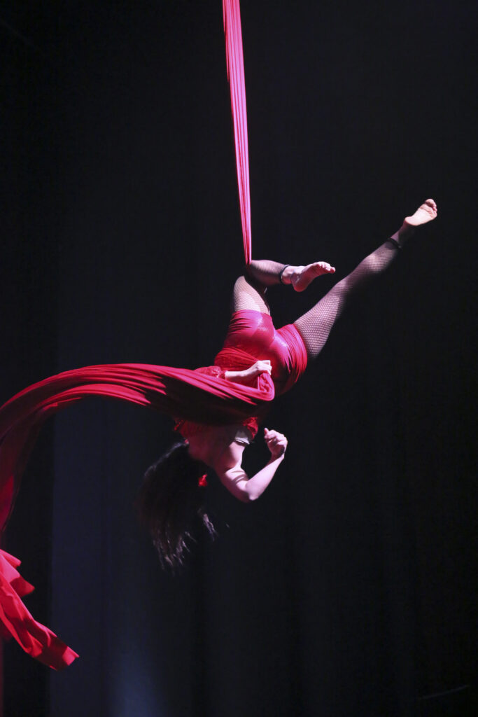 Artista acrobatica sospesa in aria, avvolta in tessuti rossi, mentre esegue una figura elegante.