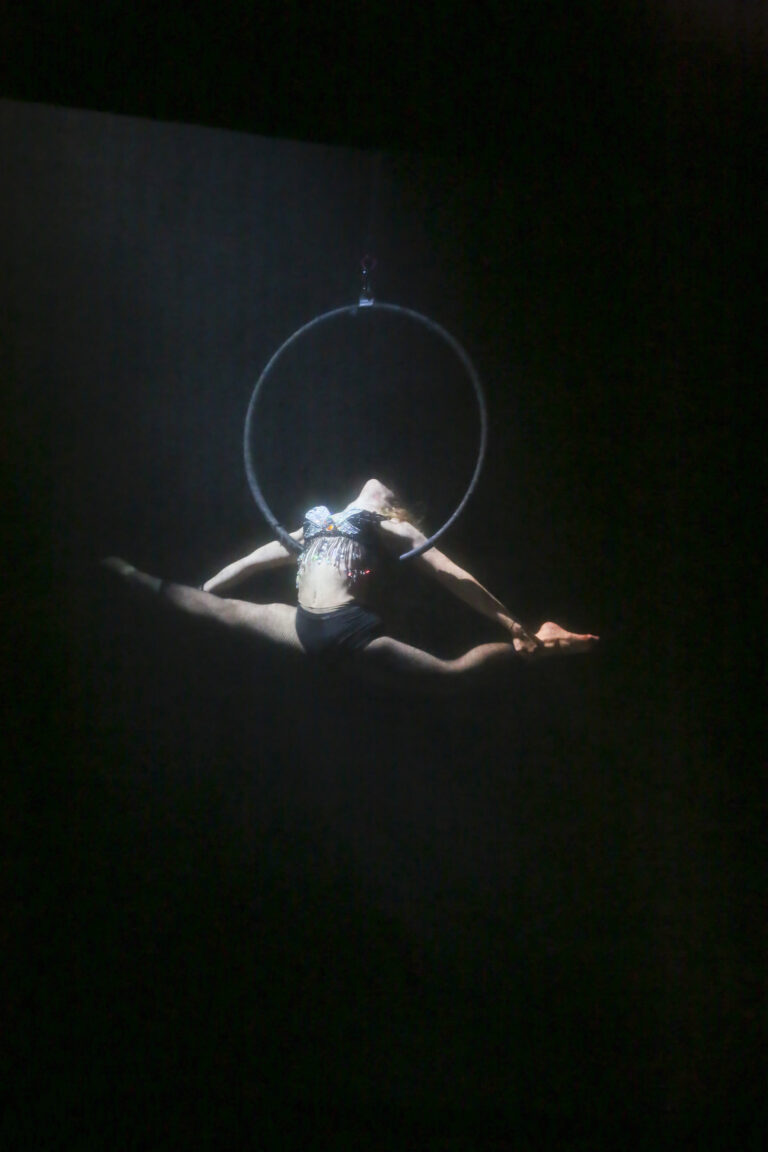Artista acrobatica in volo, sospesa in un cerchio, esegue una mossa elegante con una gamba distesa.