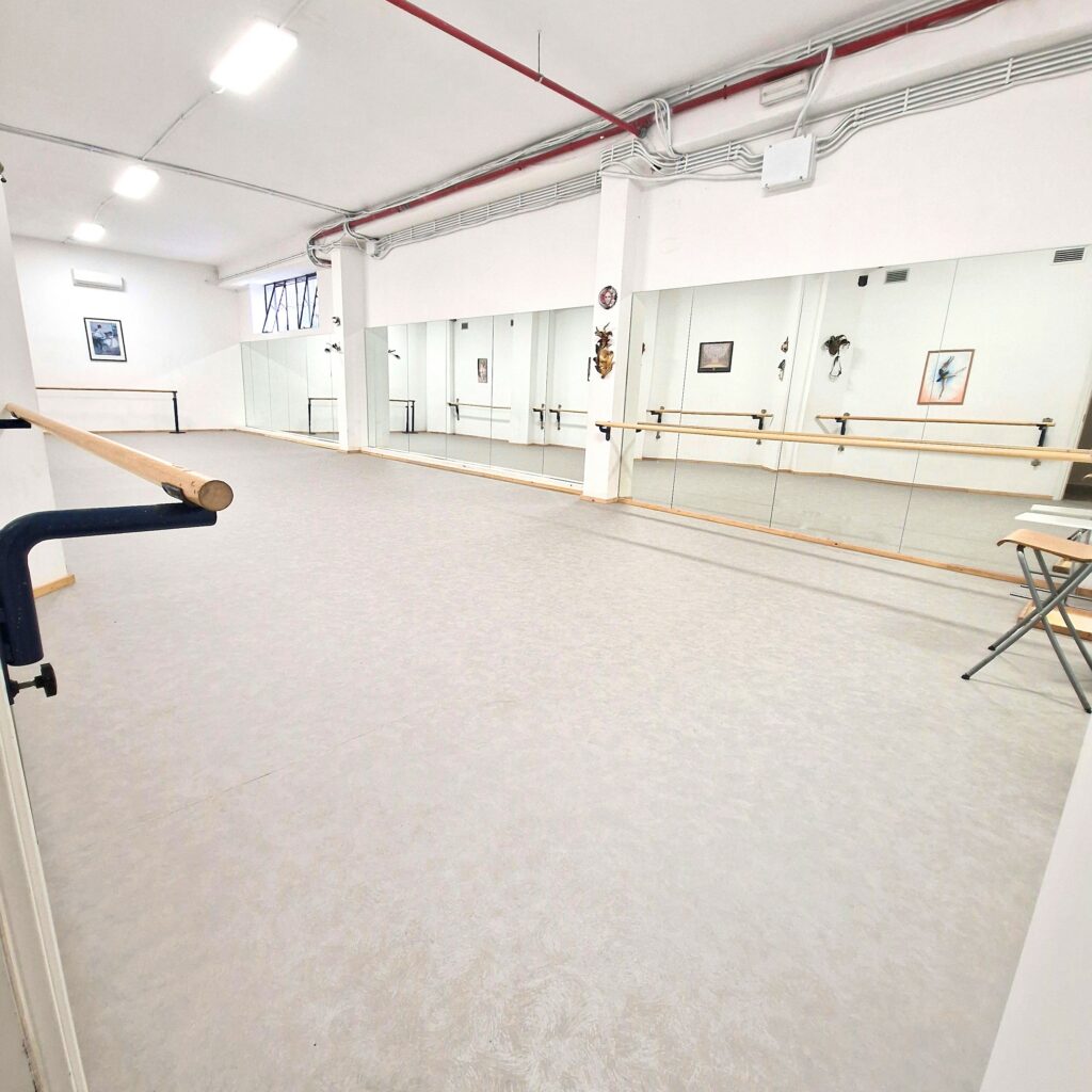 Spazio ampio e luminoso con specchi e barre per la danza, pavimento chiaro e pareti bianche.