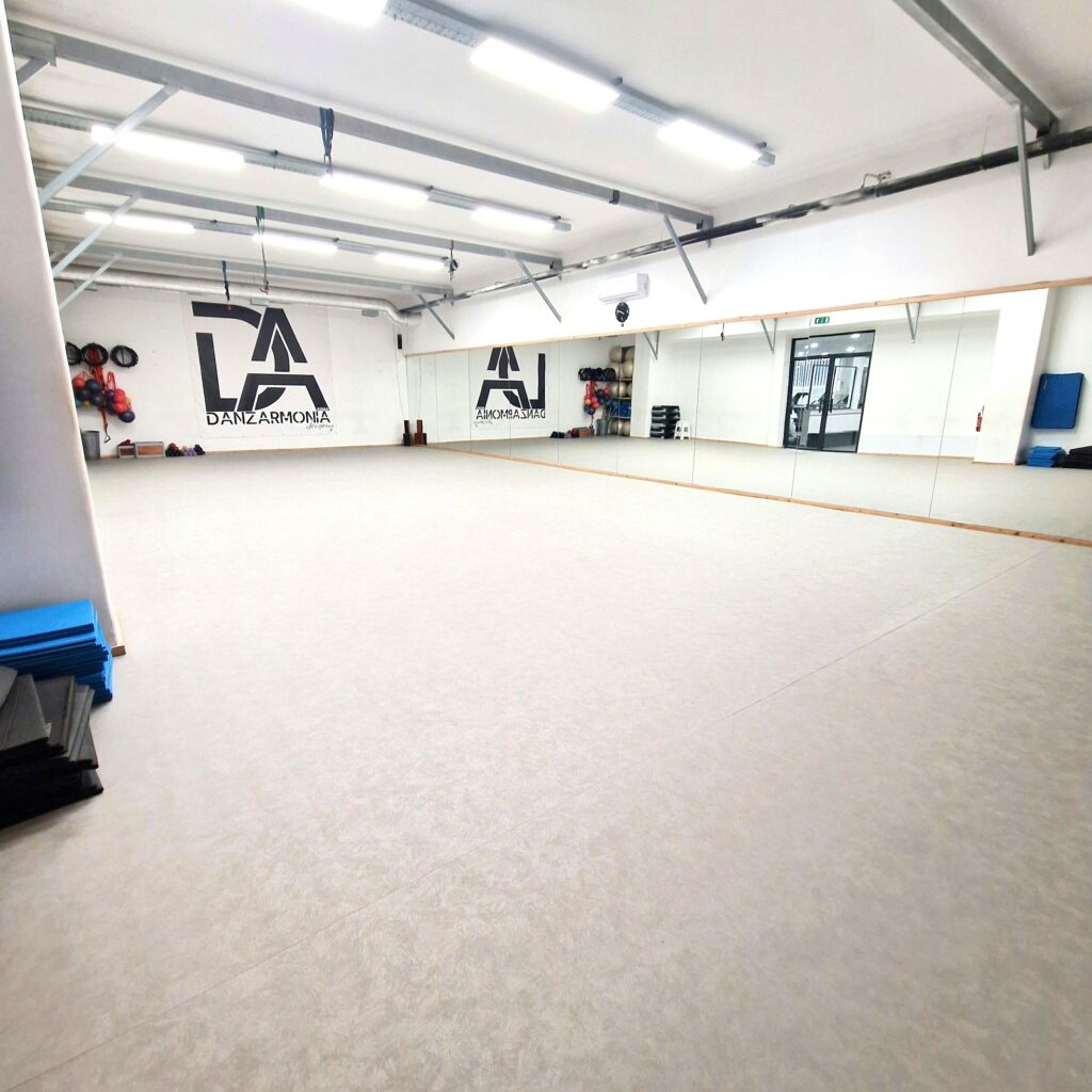 Spazio ampio e luminoso con specchi, attrezzature e pareti bianche, ideale per attività di danza.